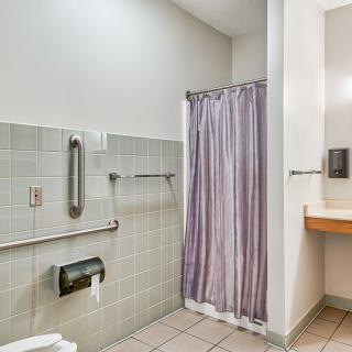 An accessible bathroom featuring a shower with a grab bar, tiled floor, and a sink with a soap dispenser.