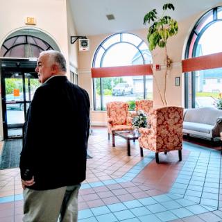 A man stands in a welcoming lobby space, featuring comfortable seating and large windows that allow natural light to fill the room.