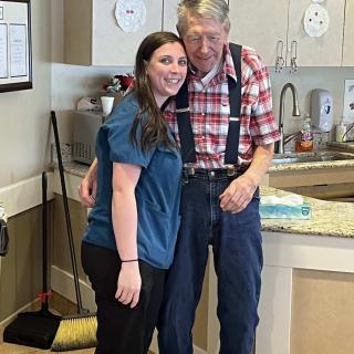 A young woman and an elderly man smiling together in a kitchen setting.