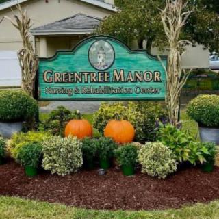 A well-maintained garden featuring a 'Green Tree Manor' sign with seasonal pumpkin decorations.