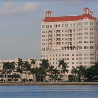 A picturesque hotel by the waterfront, surrounded by palm trees.