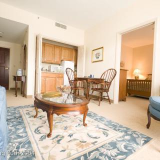 A cozy living room with a coffee table and rug, adjacent to a dining area and kitchenette in an apartment.