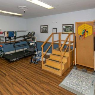 A rehabilitation room equipped with exercise equipment, including a treadmill and stairs, designed for physical therapy sessions.