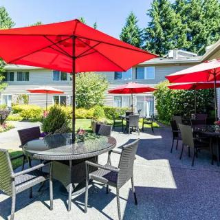 A sunny patio with tables and chairs under vibrant red umbrellas.