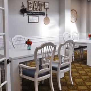 A cozy dining area with white chairs and tables, decorated with flowers and wall art.