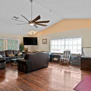 A spacious living room with comfortable seating, a large TV, and a ceiling fan.
