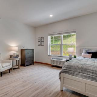 A modern and minimalist bedroom with a bed, chair, and large window.