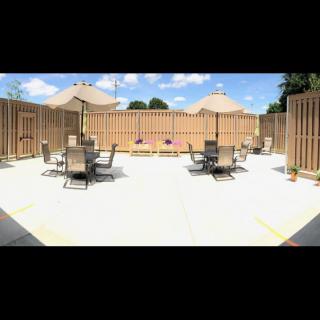 A sunny outdoor patio area with tables, chairs, and umbrellas surrounded by a wooden fence.