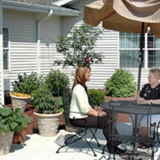 Two people sitting at a patio table under an umbrella, surrounded by plants.