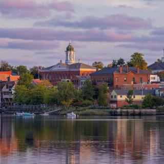 A picturesque view of a town with its buildings reflecting on the calm river under a cloudy sky.