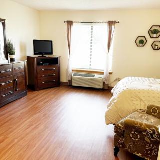 A cozy bedroom with wood flooring, featuring a bed, dresser, television, and window.