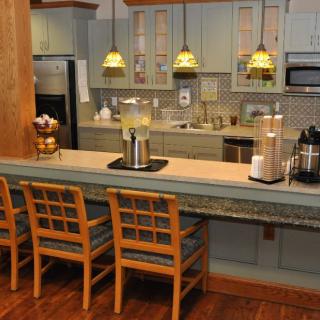 A modern kitchen with a bar counter and three wooden stools, featuring pendant lighting and stainless steel appliances.
