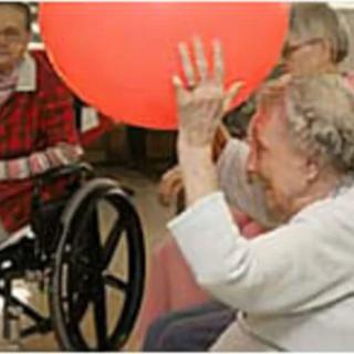 Elderly individuals engaging in a group activity with a large red ball.