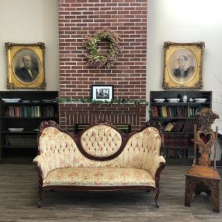 A cozy vintage interior featuring an elegant sofa and classic portraits on a brick wall.