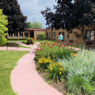 A beautifully landscaped garden with a winding pathway, surrounded by vibrant flowers and trees, leading to a building.