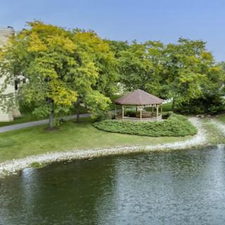 A peaceful gazebo by the lake surrounded by lush trees.