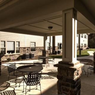 A covered patio area with tables and chairs, situated outside a building on a sunny day.