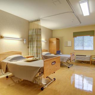 A hospital room with two beds, medical equipment, and a window.