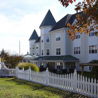 A white residential building with a pointed roof and a surrounding picket fence.