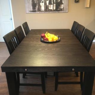 A dining room setup with a dark wooden table, surrounded by chairs and a fruit bowl centerpiece.