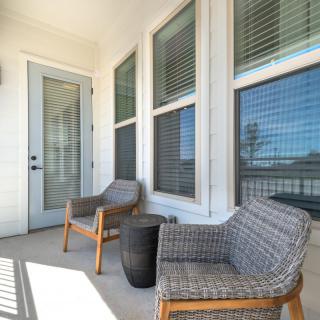 A cozy patio with two woven chairs and a small table next to large windows.