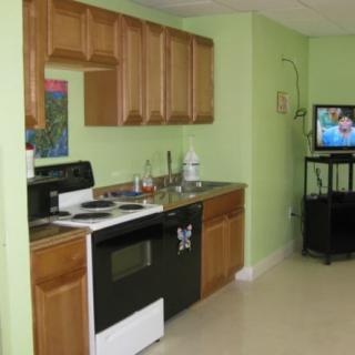 A small kitchen area with wooden cabinets and green walls, featuring an oven, sink, and a television nearby.