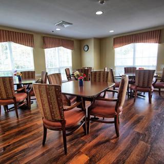 A spacious dining area with wooden tables and chairs, large windows, and curtains.