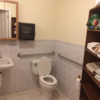A clean and organized bathroom with a toilet, sink, and shelving stocked with towels.