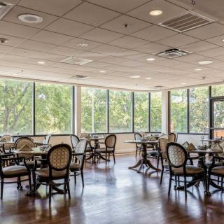 An empty restaurant dining area with tables and chairs, illuminated by natural light through large windows.