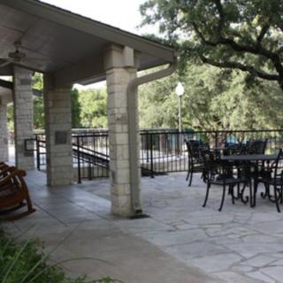 An inviting outdoor patio with seating under a covered area, surrounded by trees.