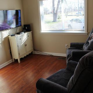 A cozy living room with armchairs facing a television and a window with blinds.