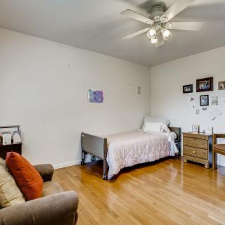 A cozy bedroom with a single bed, hardwood floors, and a ceiling fan.