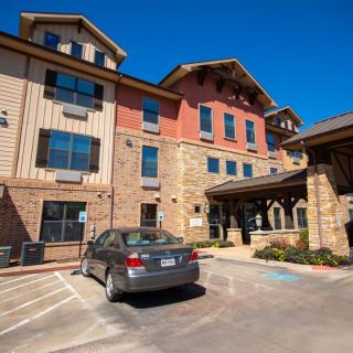 A hotel building with a car parked in the adjacent parking lot on a sunny day.