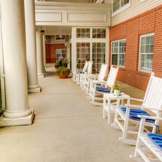 A serene porch with white rocking chairs lined up next to a brick building.