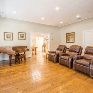A spacious living room featuring hardwood floors, a grand piano, and comfortable recliner chairs.