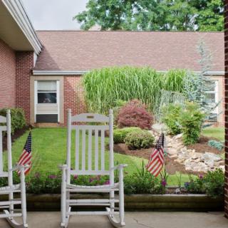 A peaceful patio with rocking chairs overlooking a well-maintained garden and small American flags.