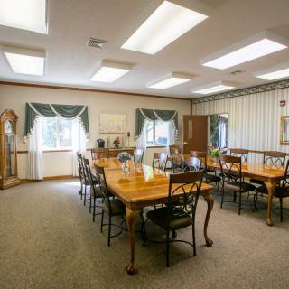 A traditional-style conference room with a large meeting table surrounded by chairs, illuminated by ceiling lights and natural light through the windows.