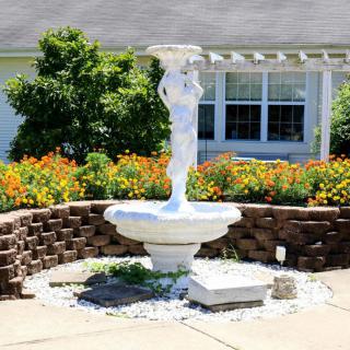 A decorative fountain with a statue centerpiece surrounded by a garden of vibrant flowers.