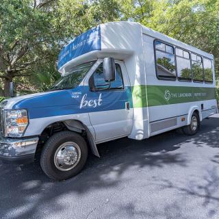 A blue and green shuttle bus parked on a sunny street surrounded by trees.