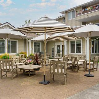A sunny patio area with tables, chairs, and umbrellas in front of a building.