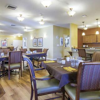 A well-lit dining area with neatly arranged tables and chairs, featuring a warm ambiance and wooden flooring.