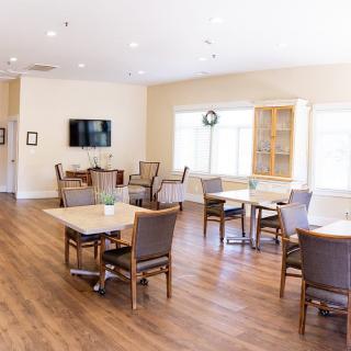 A bright dining area with hardwood floors, featuring tables and chairs, and a television on the wall.