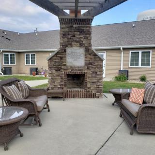 An outdoor patio setting with wicker furniture and a brick fireplace, situated near a building.