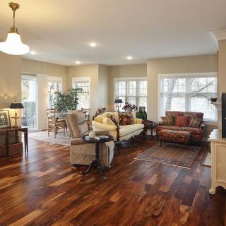 A spacious living room with hardwood floors, featuring comfortable seating and large windows.