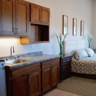 A cozy room featuring a small kitchenette with wooden cabinets and a comfortable bed.