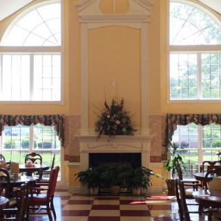 A spacious dining area with large windows and a central fireplace, featuring several tables and chairs.