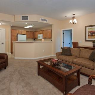 A cozy living room with an open floor plan connected to the kitchen, featuring comfortable seating and warm lighting.