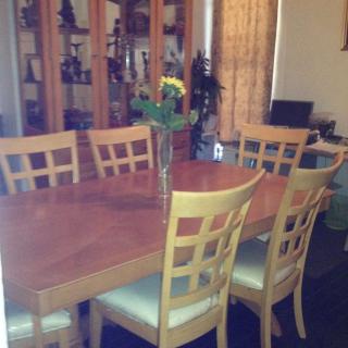 A wooden dining table set with chairs and a vase of flowers in a living room.