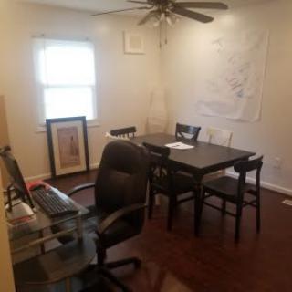 A home office with a desk, chair, and table set up near a window.
