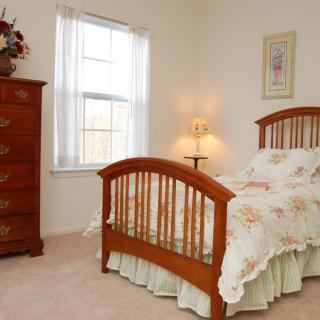 A cozy bedroom with a wooden bed and dresser, softly lit by a lamp near the window.